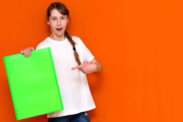 赤いスタジオの背景にバナー広告で明るい緑のフォルダを保持し 突いている白人の若い長い髪の少女を驚かせた コピースペースバナー — ストック写真