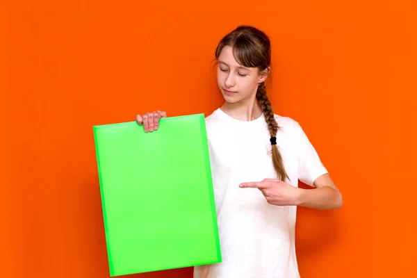 オレンジ色のスタジオの背景にバナー広告で明るい緑のフォルダを保持し 突いている白人の若い長い髪の少女を驚かせた コピースペースバナー — ストック写真