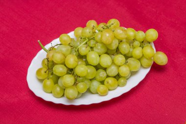 Beyaz tabakta yeşil üzüm. Kırmızı arka plan. Üst görünüm.