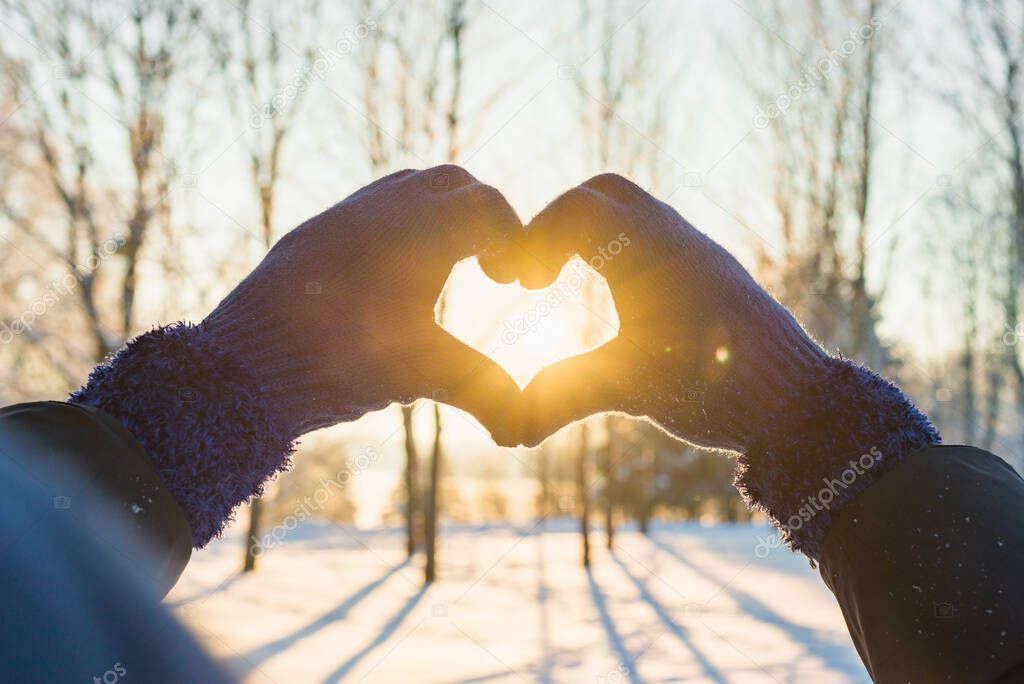 Woman making heart symbol with hands wearing gloves, sunny winter evening, sunrays, Valentines day, Love concept.