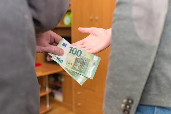 Hand giving money like bribe or tips or salary hard worked hand taking 100 euro banknotes.