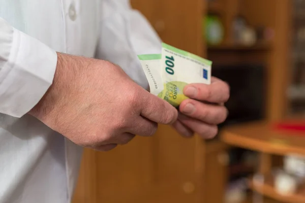 Doctor counting money 100 Euro banknotes. Paid medical services healthcare concept.