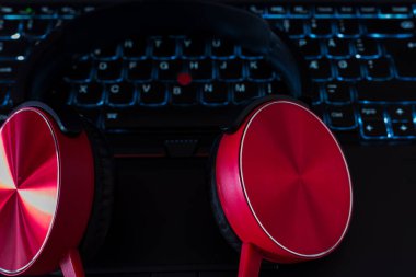 Kırmızı kulaklıklar, dizüstü bilgisayar tuşuna yaslan. Siyah mavi tuş tahtası. Görüntüyü kapat..