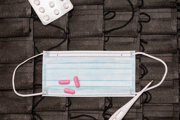 Protective medicine mask,thermometer and pills on pile black face masks background. flat lay top view.