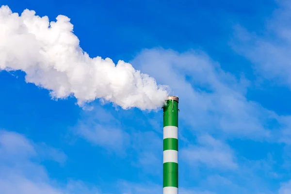 One Industrial smoke pipe from chimney on blue cloudy sky.White smoke emanates from the pipe.