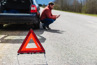 Arabası bozulduğunda yardım istemek için akıllı telefonu kullanan çömelmiş bir adam. Acil durum işaretine odaklan..