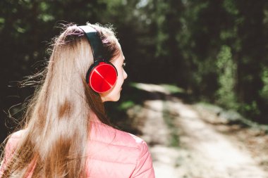 Sevimli, neşeli, sıska, eğlenen, ormanda müzik dinleyen bir genç kız yaz, bahar günü ormanı ya da park. Arka manzara, yakın çekim..