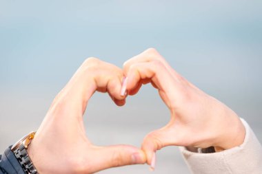 Mavi denizin arka planında kalp şeklinde erkek ve kadın elleri. Seyahat, turizm, ilişki ve mutluluk kavramı.