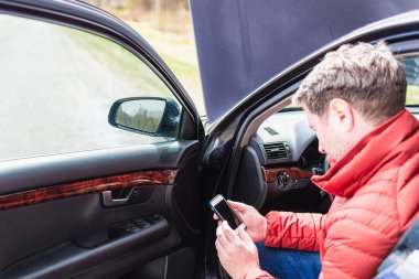Arabası bozulduğunda yardım istemek için akıllı telefonu kullanan bir adam. Telefona odaklan..