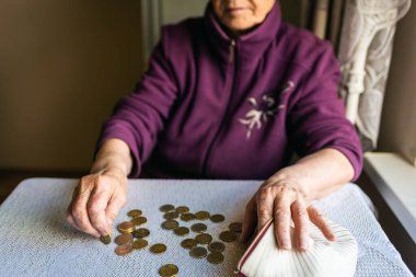 Endişeli yaşlı kadın evde oturuyor ve kalan paraları sayıyor. Yaşlı kadın evde zavallı bir şekilde masada oturuyor ve faturaları ödedikten sonra cüzdanından geriye kalan paraları sayıyor.