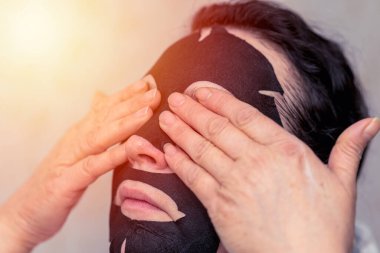 Genç bir kadın evde siyah kozmetik yüz maskesi takıyor. Yüz soyma maskesi, güzellik tedavisi, cilt bakımı, kozmetoloji. Yakın çekim..