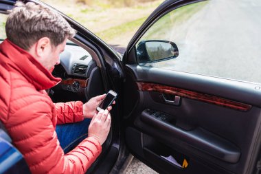 Arabası bozulduğunda yardım istemek için akıllı telefonu kullanan bir adam. Telefona odaklan..