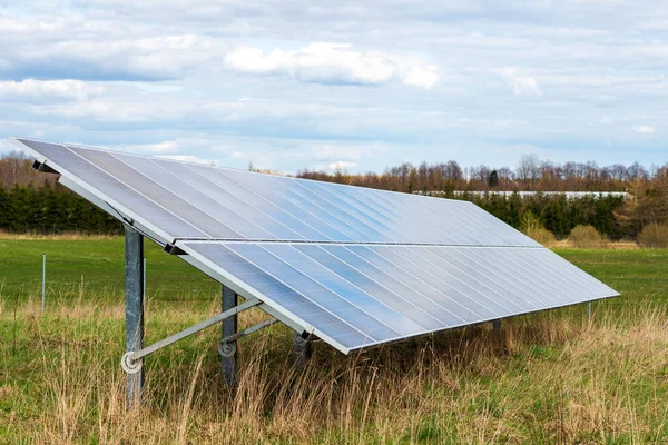 Solar panels in a field.Long line of solar electric generation panels on rural meadow near the village.Cloudy evening sky background.