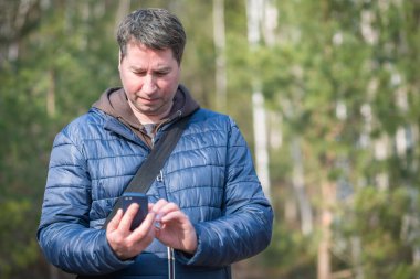 40 'lı yaşlarda cep telefonlu bir adam bahar ormanlarında sinyal arıyor..