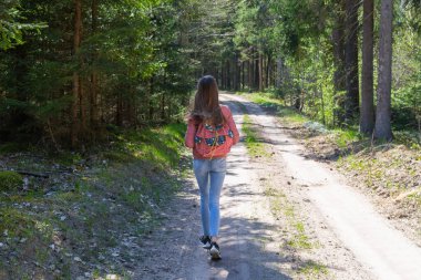 Sırt çantalı genç bir kız turist yaz günü ormanda yürüyor. Hipster yaşam tarzı ve tek kişilik gezi..