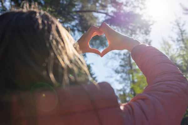 Hands in heart shape. Teenage girl hands heart shape on against blurry forest background of summer or spring.Closeup