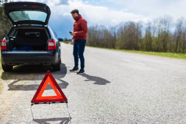 Arabası bozulduğunda yardım istemek için akıllı telefonu kullanan bir adam. Acil durum işaretine odaklan..