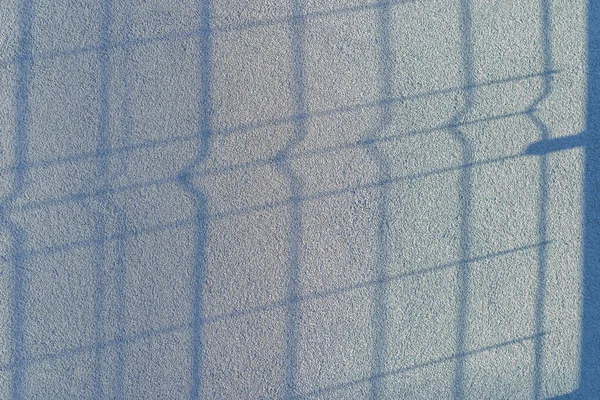 The shadow of the fence on the gray blue plastered wall. Fence with sunlight and shade. Modern design. Shadows from grid lines or fence grates or railings. copy space.