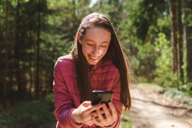 13. yaş gününün bir kızı ormandaki arkadaşına video görüşmesi yapıyor. Çevrimiçi iletişim konsepti. Güneşli bir bahar ya da yaz günü..