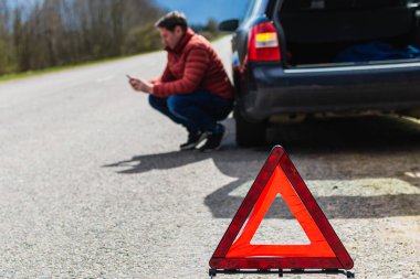 Arabası bozulduğunda yardım istemek için akıllı telefonu kullanan çömelmiş bir adam. Acil durum işaretine odaklan..