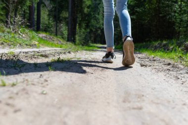 Kadın turist bacakları ve spor ayakkabıları orman yolunda yürüyor. Gün ışığı..
