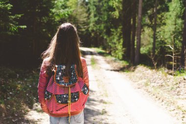 Sırt çantalı genç bir kız turist yaz günü ormanda yürüyor. Hipster yaşam tarzı ve tek kişilik gezi..