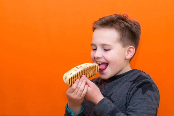 ハンサムな10歳の男の子は熱い犬を屋内オレンジのスタジオの背景画像を保持し — ストック写真