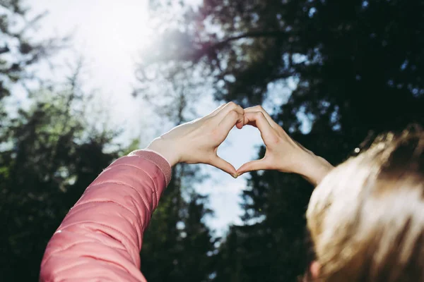 Hands in heart shape. Teenage girl hands heart shape on against blurry forest background of summer or spring.Closeup