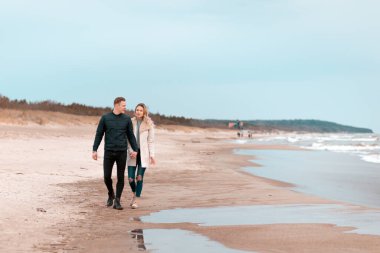 İlkbahar romantik tatilinde kumlu bir plajda, açık havada yürüyen çekici genç bir çift. Seyahat eden turistlerin yaşam tarzı. Çiftler birlikte eğleniyorlar..