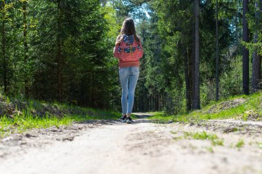 Sırt çantalı genç bir kız turist yaz günü ormanda yürüyor. Hipster yaşam tarzı ve tek kişilik gezi..