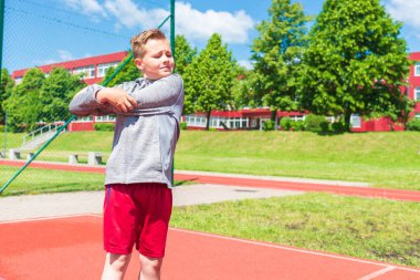 Basketbolcu çocuk sahada esneme hareketleri yapıyor. Çocuk ısınıyor. Güneşli bir günde Red Court Sokağı 'nda..