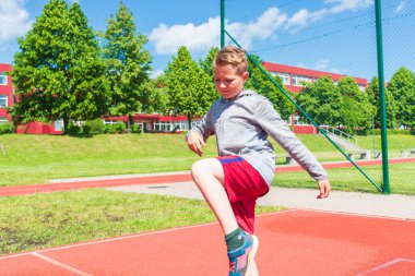 Basketbolcu çocuk sahada esneme hareketleri yapıyor. Çocuk ısınıyor. Güneşli bir günde Red Court Sokağı 'nda..