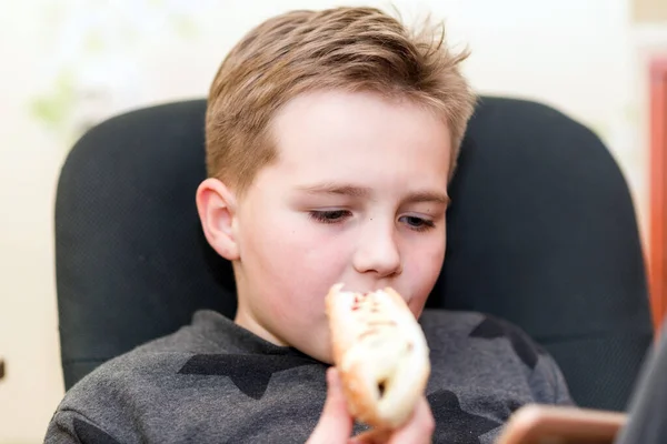 Głodny Chłopiec Jedzący Hot Doga Domu Siedzi Podczas Zabawy Smartfonem — Zdjęcie stockowe