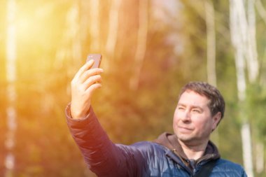 40 'lı yaşlarda cep telefonlu bir adam güneşli bahar ormanlarında sinyal arıyor..