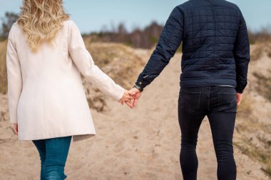 Kum tepelerinde el ele yürüyen genç bir çift. Uzakta, ormanda. Macera yolculuğu yaşam tarzı konsepti..