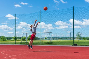 Çekici genç çocuk oyun sahasında potaya top atıyor. Tatlı çocuk yaz aylarında oyun bahçesinde basketbol oynuyor..