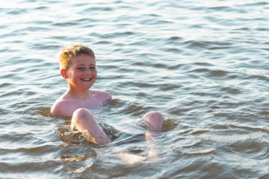 Mutlu gülümseyen çocuk suda yüzerken eğleniyor. Tatlı çocuk suda yüzüyor. Çocuk sahilde eğleniyor. Yaz tatili. Aktif yaşam tarzı konsepti. Yaz tatilindeki mutlu çocuk..