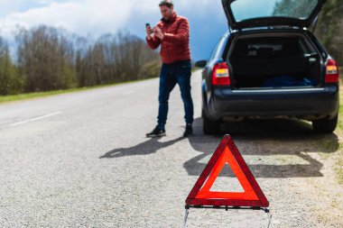 Arabası bozulduğunda yardım istemek için akıllı telefonu kullanan bir adam. Acil durum işaretine odaklan..