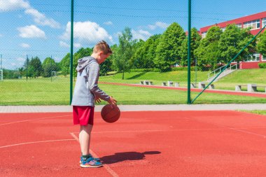 Çocuk oyun sahasında basketbol atışına hazırlanıyor. Çocuk güneşli yaz günlerinde oyun sahasında basket oynuyor..