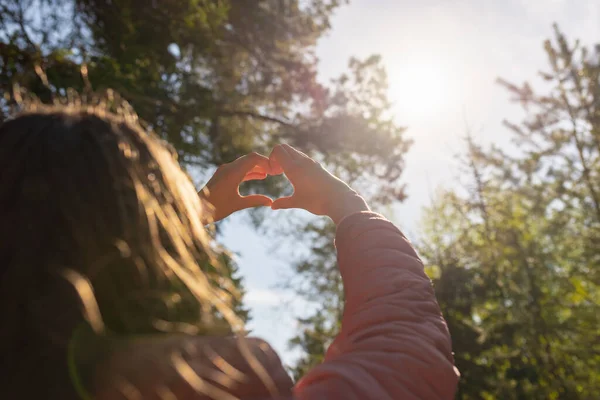 Hands in heart shape. Teenage girl hands heart shape on against blurry forest background of summer or spring.Closeup