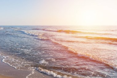 Güzel gün batımı ya da sahilde gün doğumu dalgaları. Mavi gökyüzü ve sakin boş sahil manzarası.