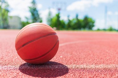 Kırmızı kauçuk bir sahada turuncu eski basketbol topu. Güneşli yaz sıcağı. Arka plan bulanık. Turuncu top oyuncuyu bekliyor..