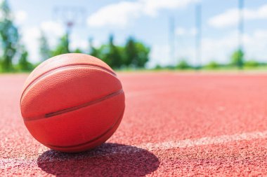 Kırmızı kauçuk bir sahada turuncu eski basketbol topu. Güneşli yaz sıcağı. Arka plan bulanık. Turuncu top oyuncuyu bekliyor..