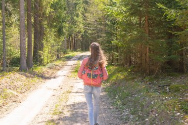 Sırt çantalı genç bir kız turist yaz günü ormanda yürüyor. Hipster yaşam tarzı ve tek kişilik gezi..