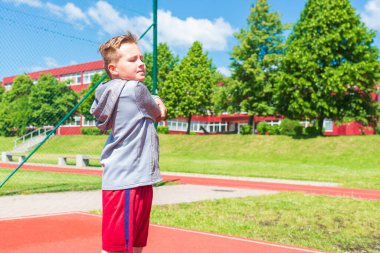 Basketbolcu çocuk sahada esneme hareketleri yapıyor. Çocuk ısınıyor. Güneşli bir günde Red Court Sokağı 'nda..