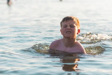Mutlu gülümseyen çocuk suda yüzerken eğleniyor. Tatlı çocuk suda yüzüyor. Çocuk sahilde eğleniyor. Yaz tatili. Aktif yaşam tarzı konsepti. Yaz tatilindeki mutlu çocuk..