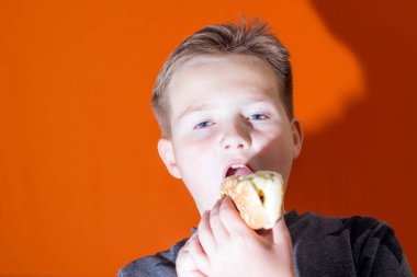 Yakışıklı, yaşlı bir çocuk içeride sosisli tutuyor ve ısırıyor. Portakal rengi stüdyo arkaplan görüntüsü. Yakından..