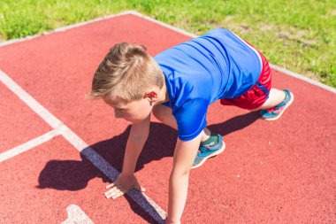 Kafkasyalı okul çocuğu kırmızı pistte koşmaya hazır ol. Başlangıç pozisyonunda koşmaya hazır genç çocuk. Sağlıklı bir yaşam tarzı..