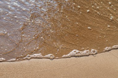 Kumlu akşam kumsalında denizin yumuşak dalgası. Odaklanma, bulanık görüntü. Boşluğu kopyala.