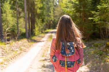 Sırt çantalı genç bir kız turist yaz günü ormanda yürüyor. Hipster yaşam tarzı ve tek kişilik gezi..